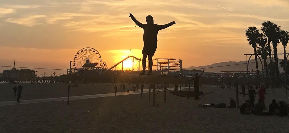 A tightrope walker on the beach at Santa Monica at sunset, with the fair on the pier in the background