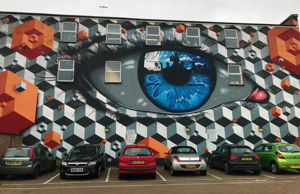 An eye, painted by My Dog Sighs, surrounded by geometric street art by Snub 23, on a wall opposite Tesco Express in Fratton, Portsmouth