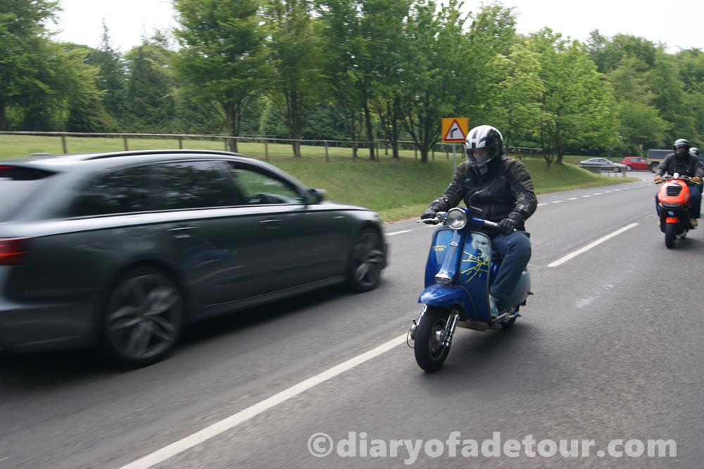 Custom Lambretta being ridden along the road, with a Hazel O'Connor theme.