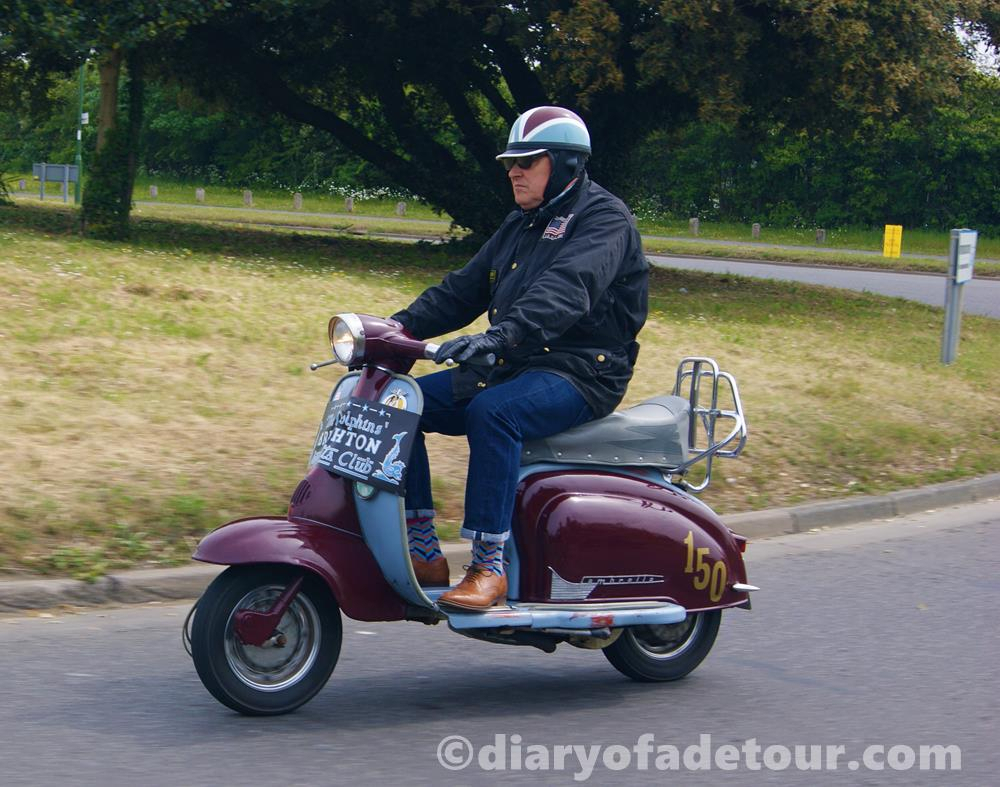 Burgundy Series 1 Lambretta being ridden by a rider with an old fashioned helmet
