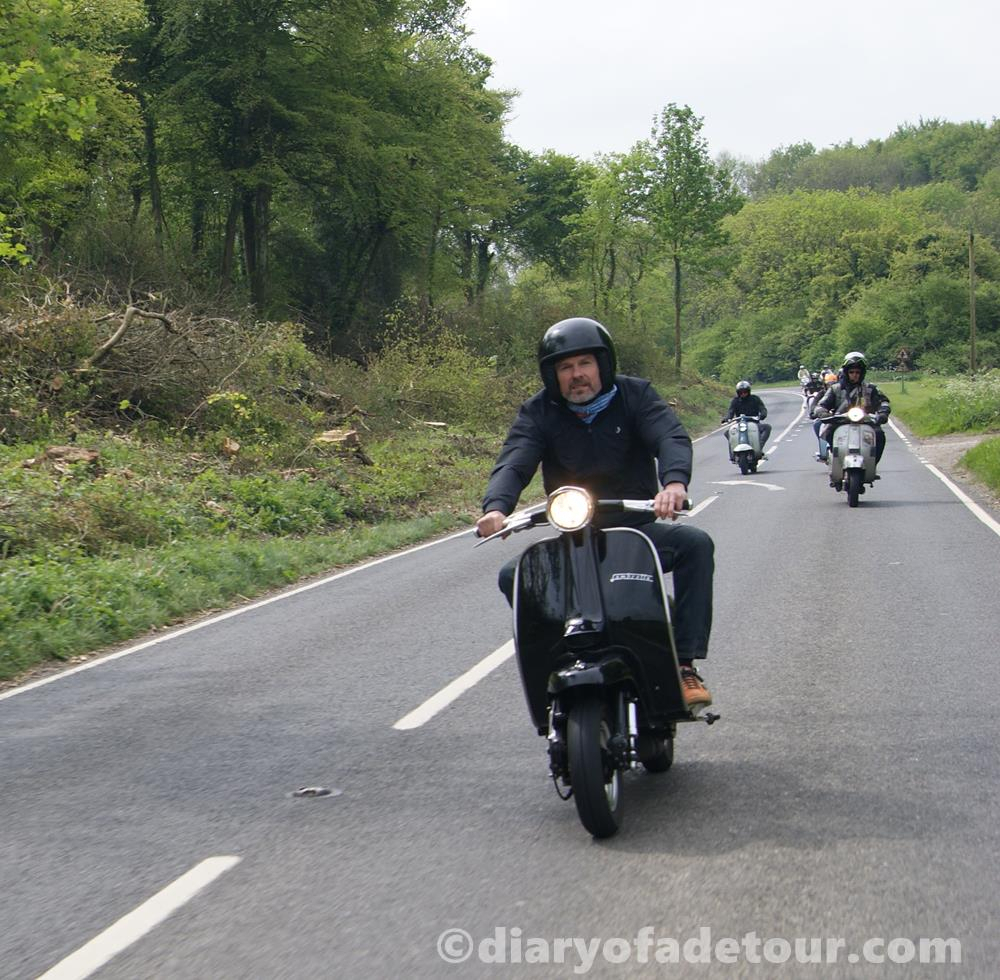Black Lambretta riding along a road with other scooters