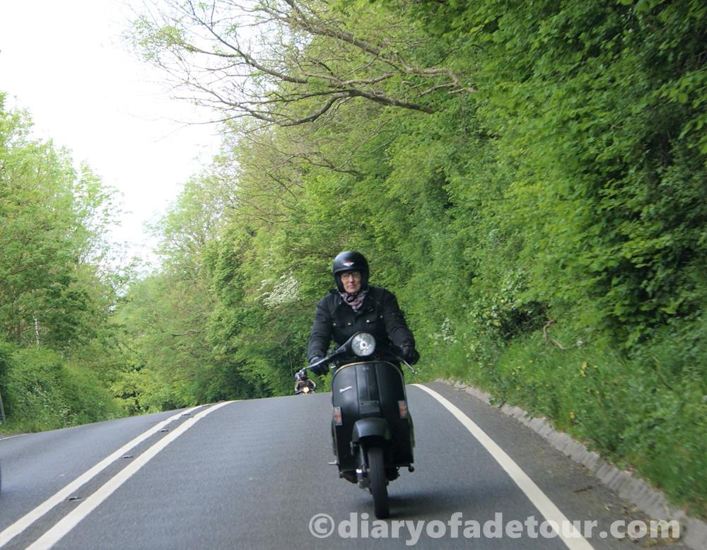 Black Vespa PX scooter riding along a country lane