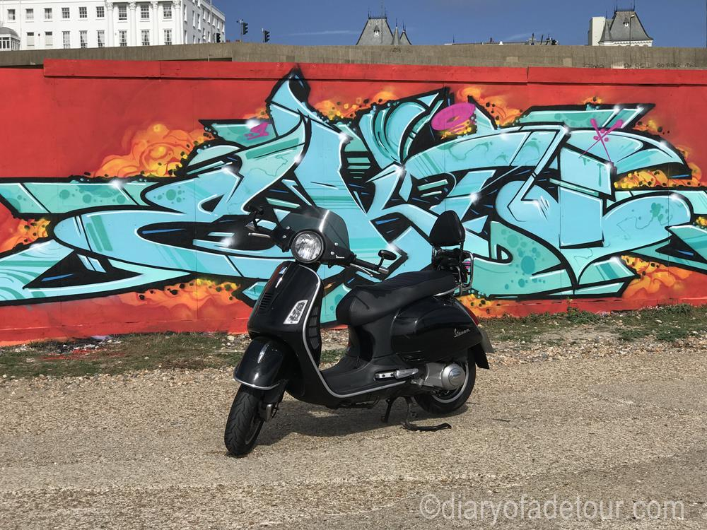 Vespa GTS in front of graffiti at Black Rock in Brighton