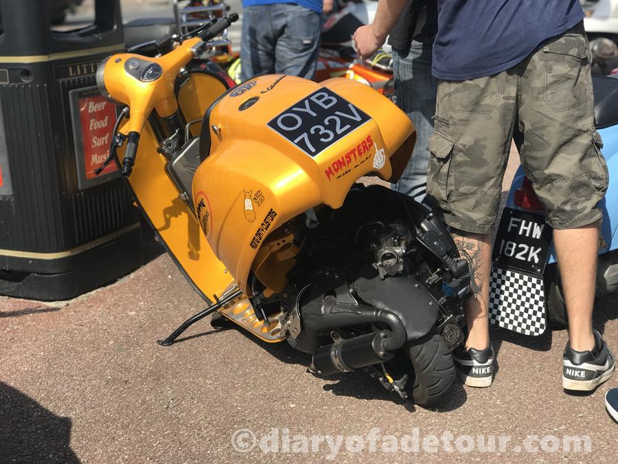 Orange scooter by Insane Innovations with the back end flipped up to see the engine.