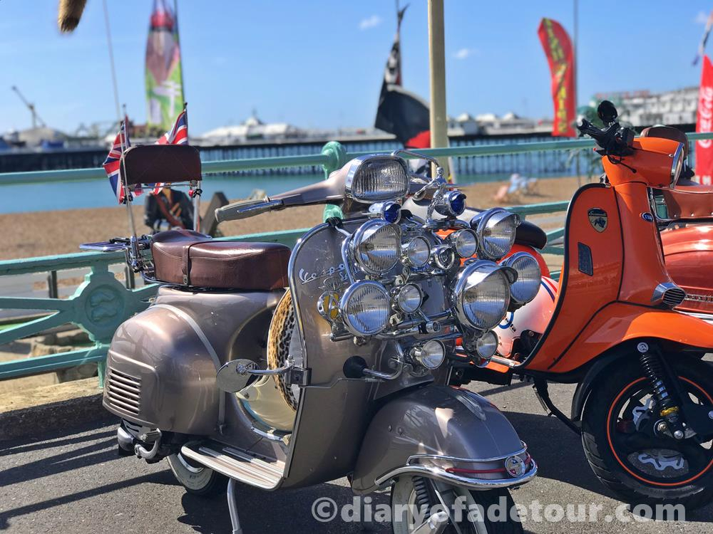 Mod scooter with lights and mirrors parked on Brighton seafront with the pier in the background