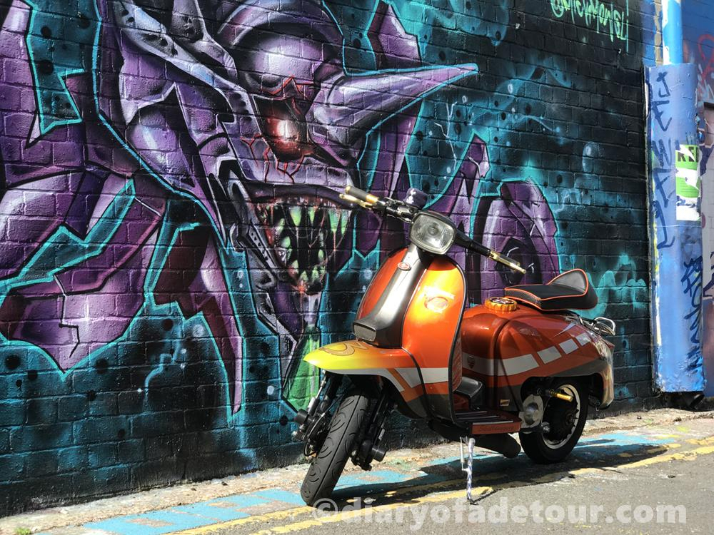 Orange street style Lambretta in front of Brighton street art by Mick Mowgli