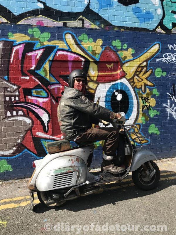 Scooter rider on a silver Vespa in front of street art in Brighton