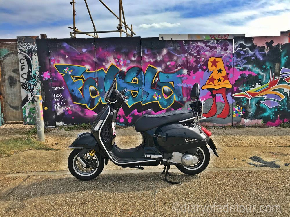 Black Vespa GTS in front of a Guy Favela mural in Brighton