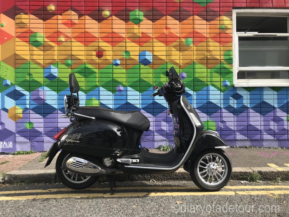 Black Vespa GTS in front of an isometric mural by Snub23 and Sprite.  The mural is in rainbow colours and was created for pride weekend.