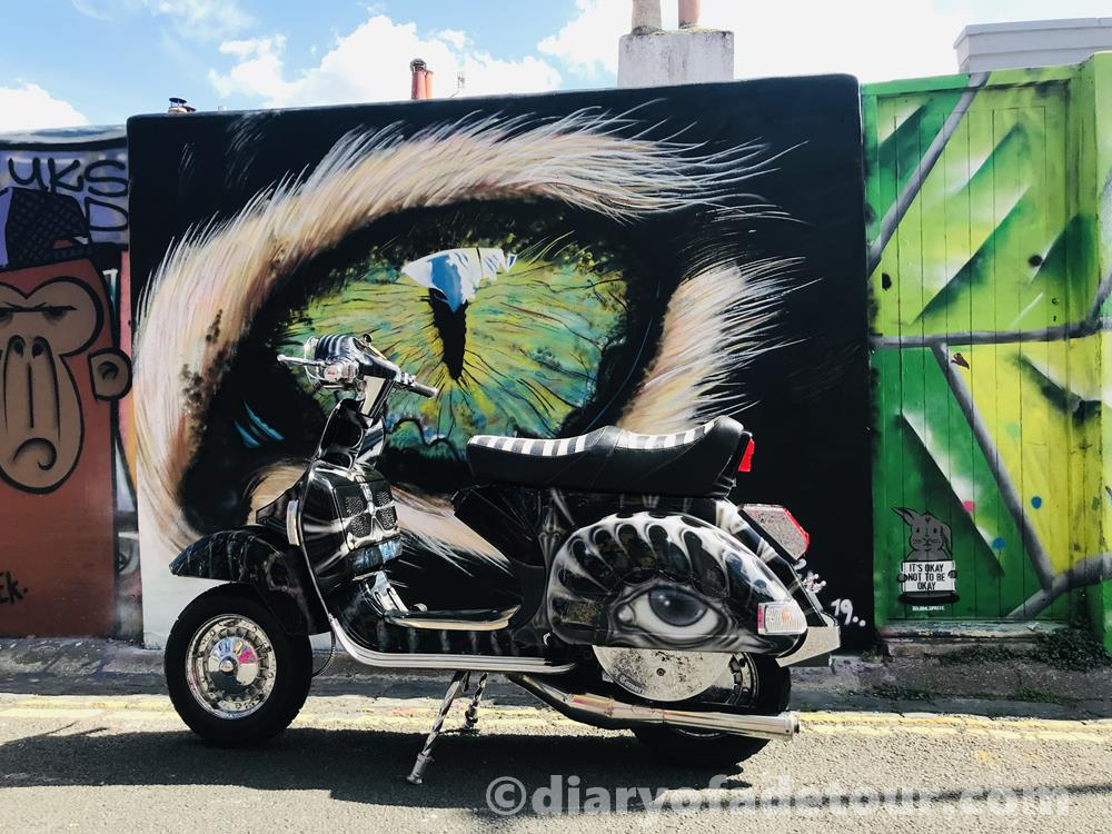 Custom Vespa, The Relic, with eye mural in front of a street art image depicting a giant eye