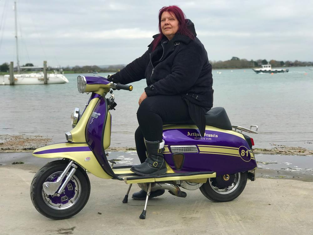 A lady sitting on a purple and gold Arthur Francis streetstyle Lambretta scooter parked at Itchenor harbour near Chichester