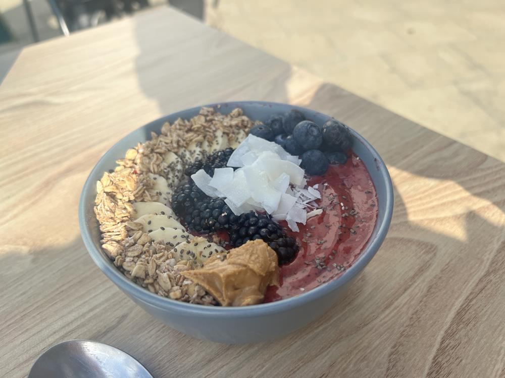 A smoothie bowl with fruit, coconut flakes, granola and chia seeds arranged on top of a berry smoothie. From the e-bike cafe in Weymouth.