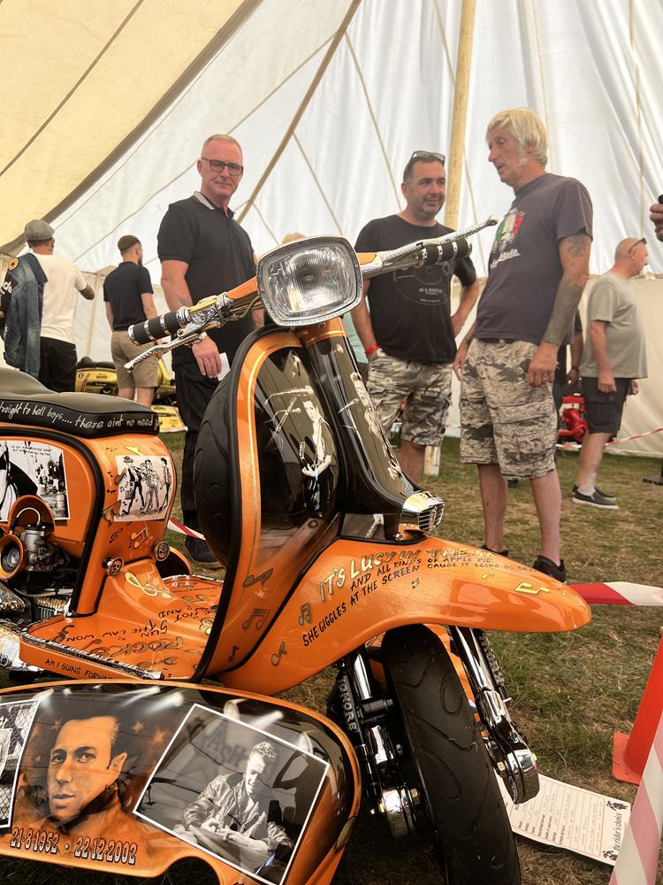 Orange Lambretta "Breaking Rocks" with murals of The Clash and owner Gary Wickham in the background.