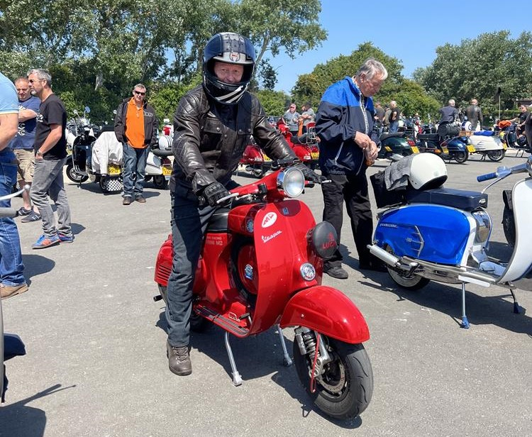 A man sitting on a red Vespa SS scooter at East Beach car park in Selsey, West Sussex.