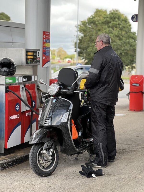 A man filling up a black Vespa GTS300 HPE2 with petrol.