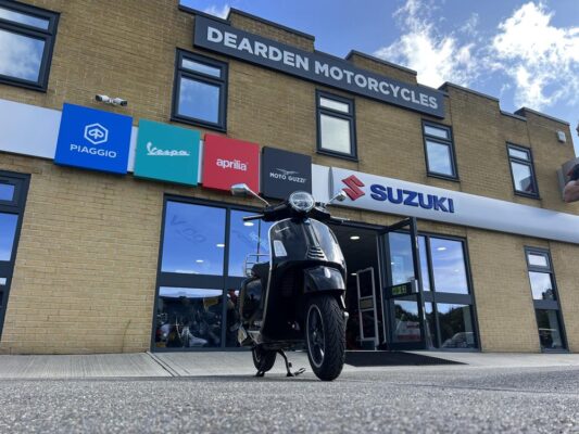 Black Vespa GTS parked outside the Dearden Motorcycles showroom.