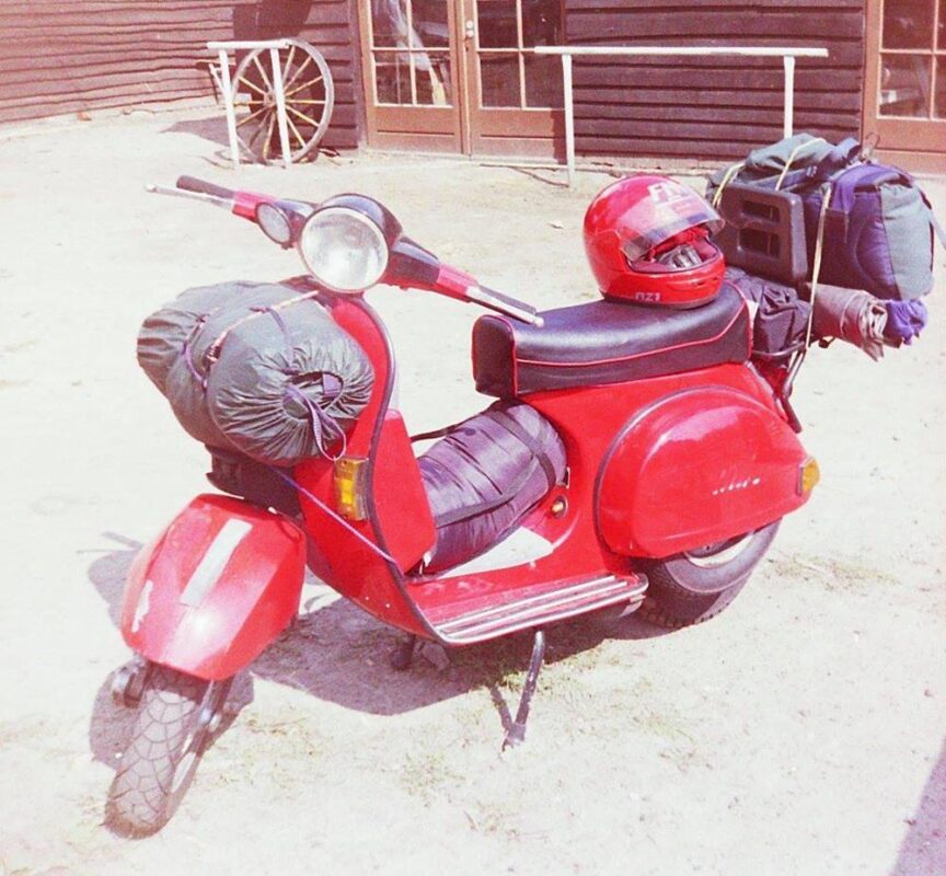 A red PX Vespa scooter with luggage on the front and back.