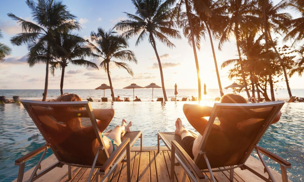 A couple laying on sunbeds as the sun is setting on a tropical holiday