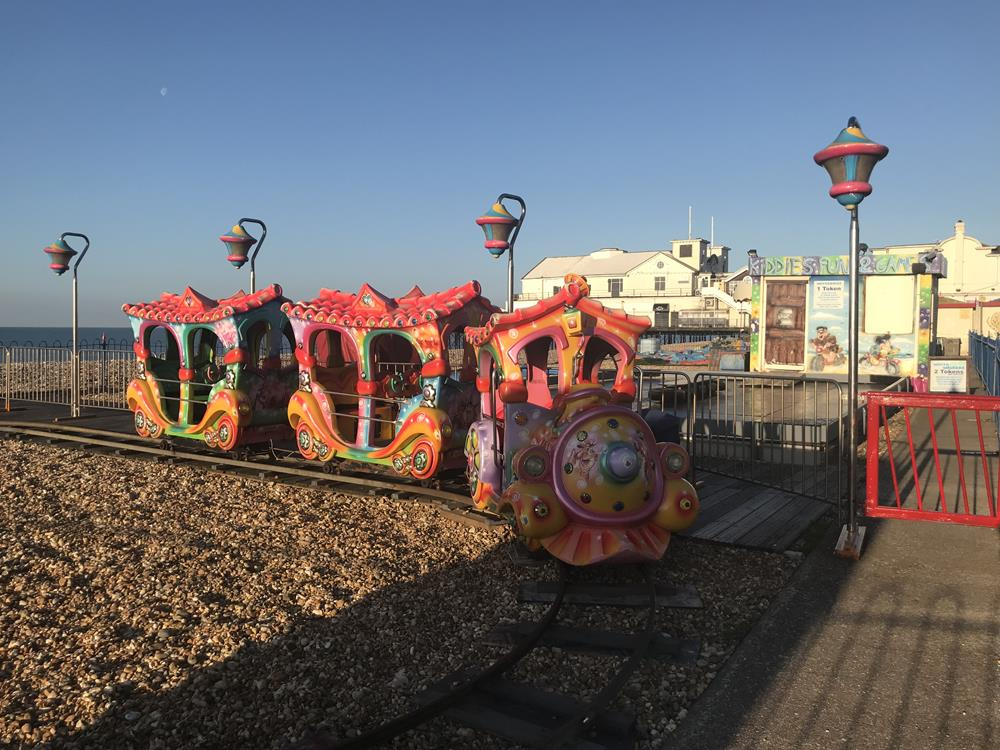Brightly coloured red and multicolour mini train on Bognor seafront with the pier in the background
